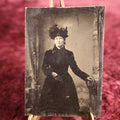 Lot 108 - Tintype - Woman Standing, Dressed In Dark Clothes With Large Decorative Hat, Leather Gloves, Leaning On Pedestal