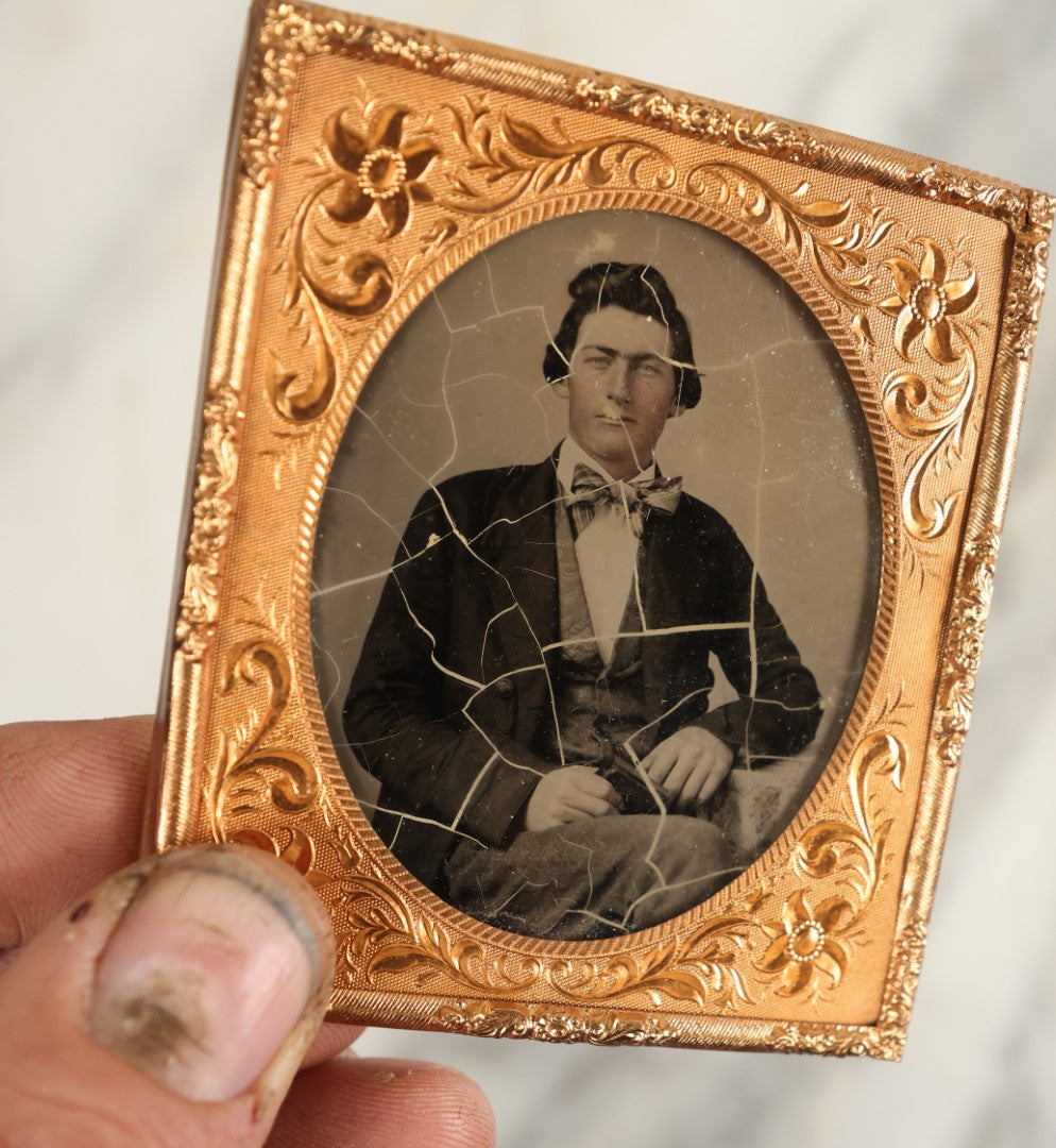 Lot 107 - Antique 1/6th Plate Ambrotype Of A Steely Eyed Young Man In A Suit And Bowtie Holding A Thermoplastic Photo Case In Lap, Note Crazing To Ambrotype Black Paint Backing, No Case