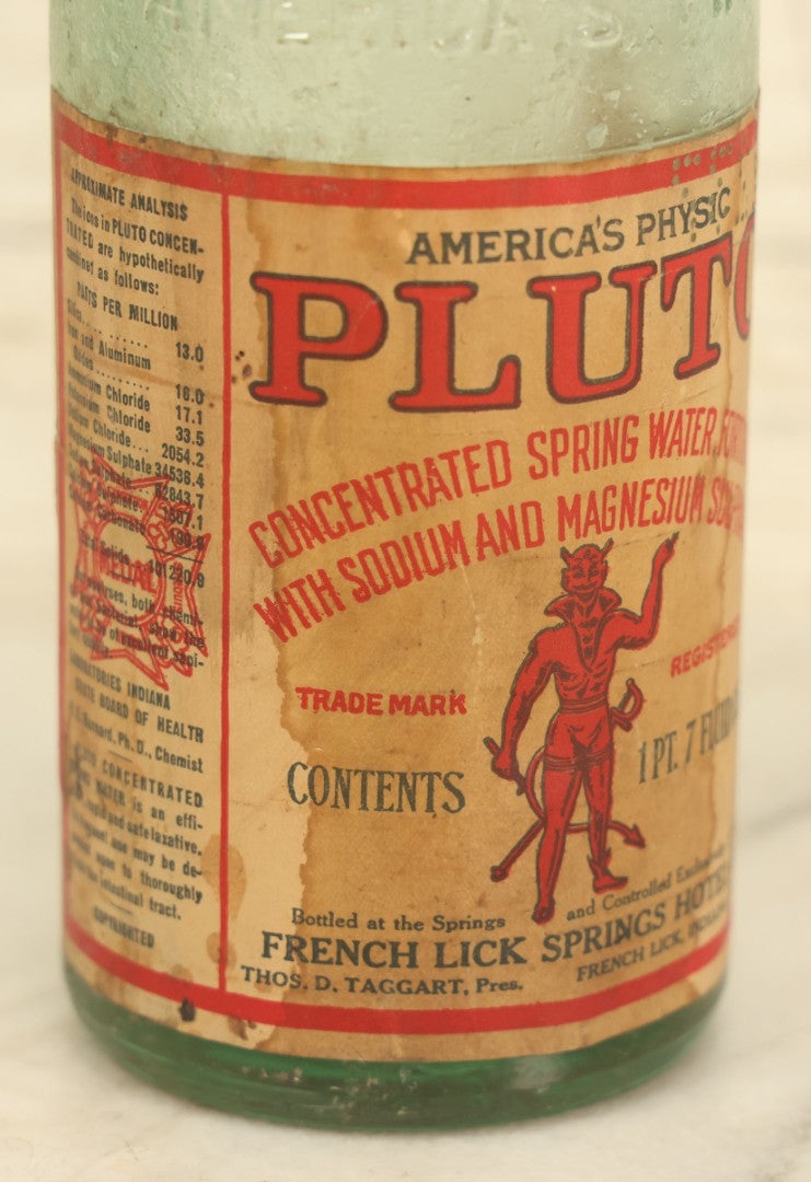 Lot 005 - Antique Pluto Water Glass Bottle With Original Paper Label, Devil Graphics, French Lick Springs Hotel Co., French Lick, Indiana, With Embossed Devil On Bottom, Drilled Cap