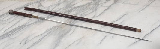 Lot 014 - Antique Wood And Metal Sword Cane, Sword Pulls Out Of Cane, With Ornate Silver Plate Topper, Note Cracks, Wear, Repairs, Approximately 35" Overall Length