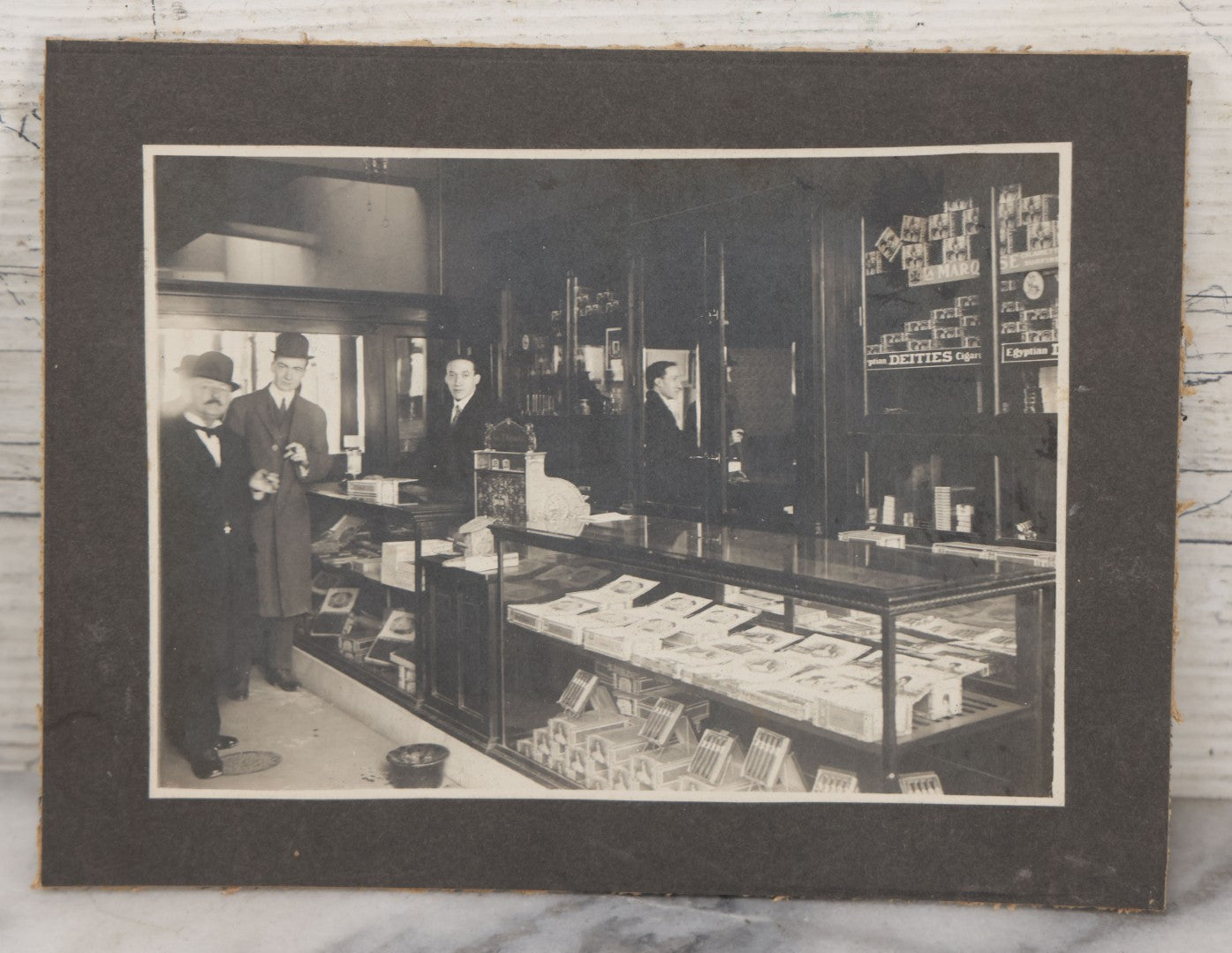 Lot 109 - Antique Boarded Photo Of A Tobacco, Cigar Shop, With Man Behind Counter, Customers In Bowler Hats, Various Cigar Brands