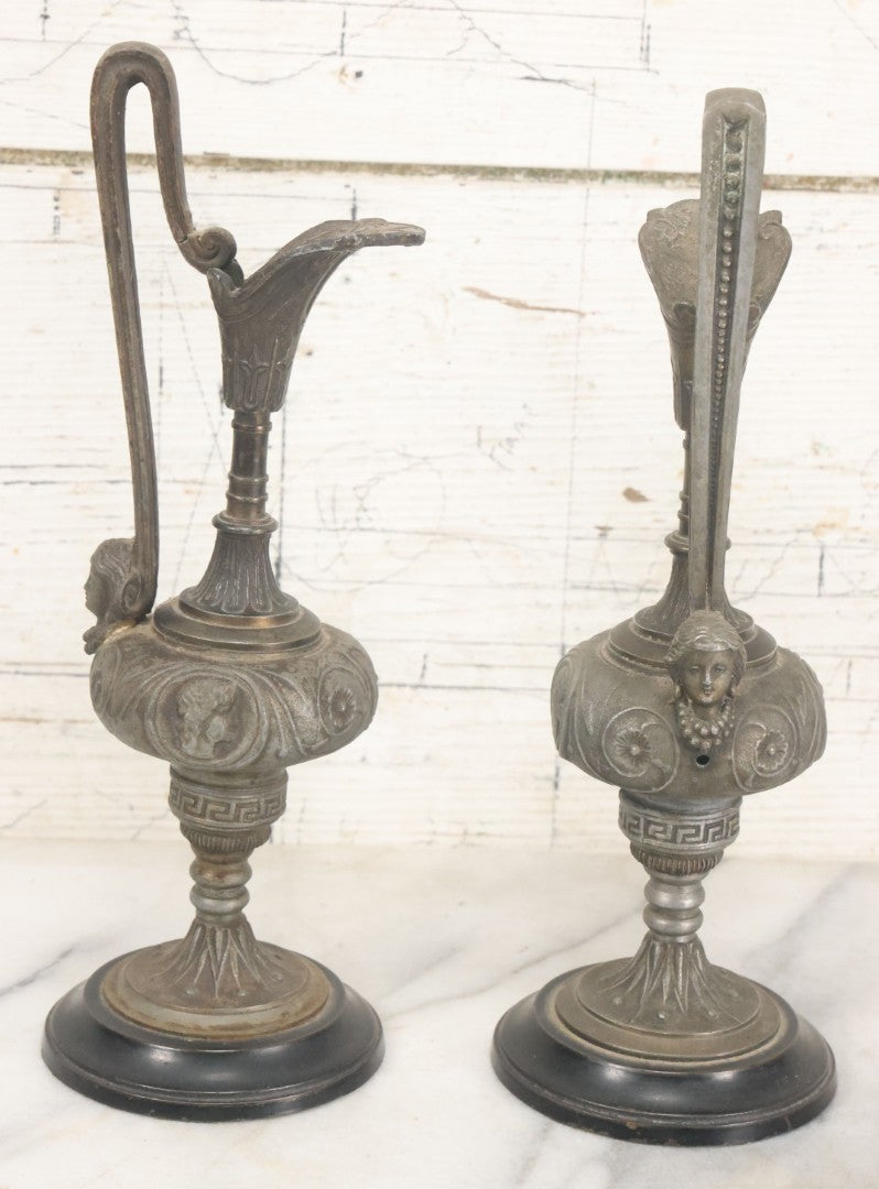 Lot 011 - Pair Of Antique Ornate Cast Pot Metal Ewers, With Woman's Head On Handle, And Woman's Head In Profile, Greek Key Design, Note Crack In Handle And Crack On Base Of One, 10-5/8" High Each