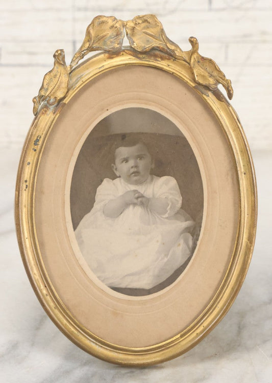 Lot 064 - Antique Oval Boarded Photograph Of Young Baby In White Gown In Brass Frame With Iris Flower Motif, 4-3/8" x 6-1/2"