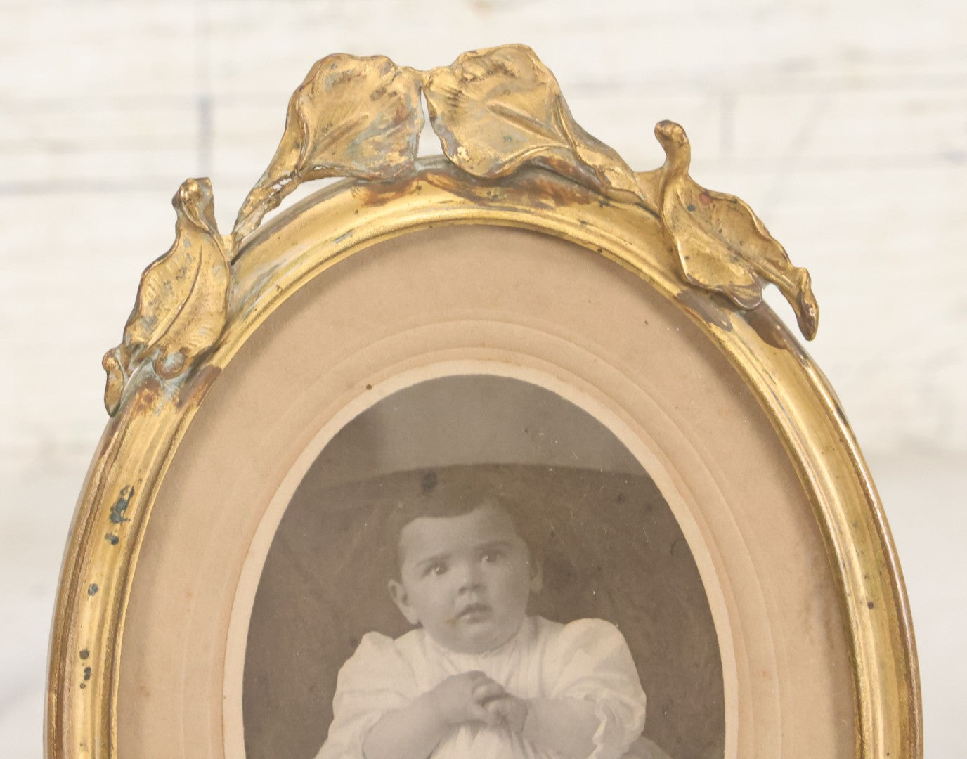 Lot 064 - Antique Oval Boarded Photograph Of Young Baby In White Gown In Brass Frame With Iris Flower Motif, 4-3/8" x 6-1/2"