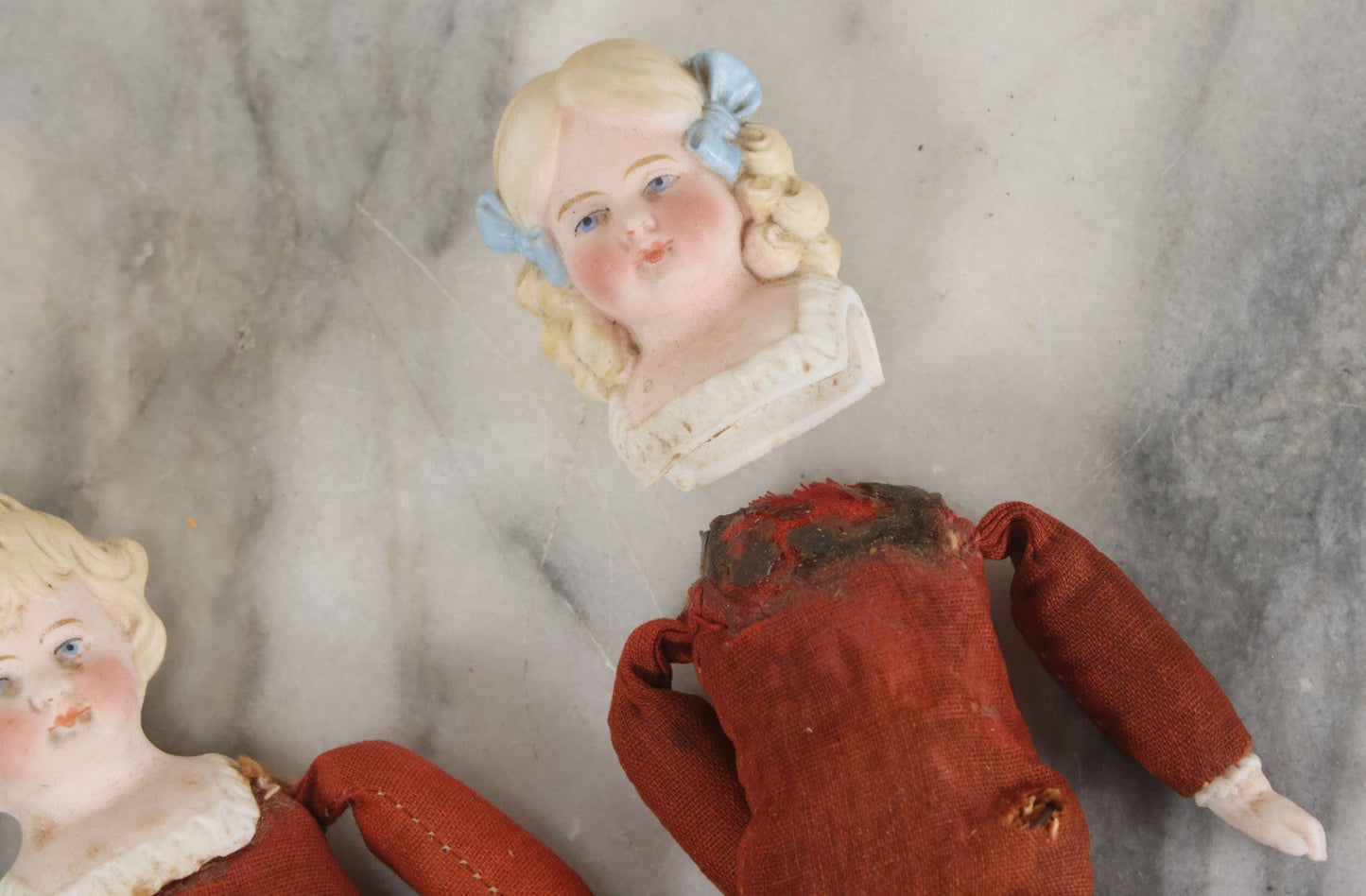 Lot 097 - Pair Of Antique Bisque Dolls With Boy And Girl With Blue Bows And Sawdust Filled Cloth Bodies, Note Girl's Head Detached, Holes In Bodies, With Sawdust Leakage, 6-1/4" Height Each