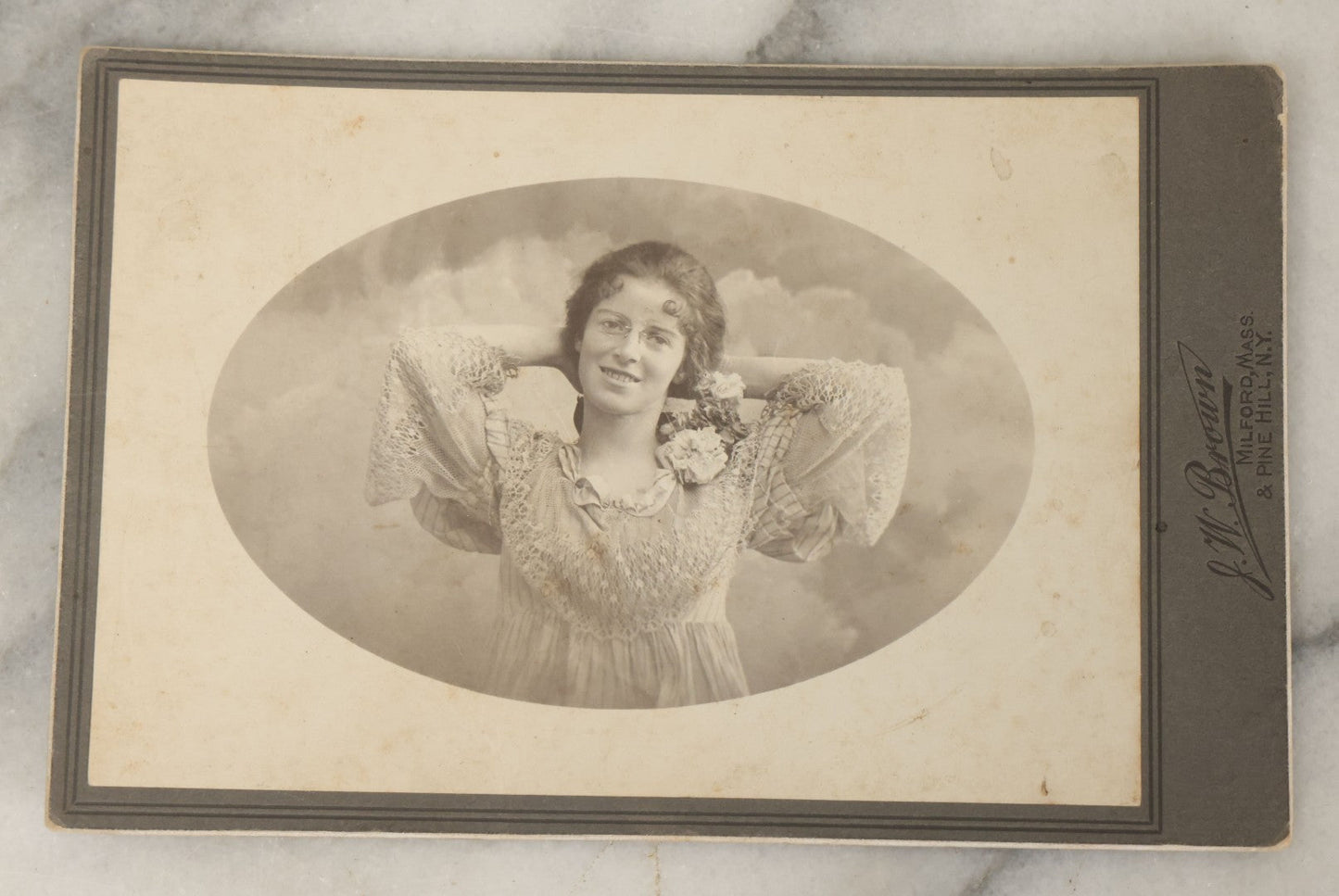 Lot 054 - Antique Cabinet Card Photograph Of A Young Woman In Glasses Posing Playfully With Hands Behind Head, J.W. Brown Photographer, Milford, Massachusetts