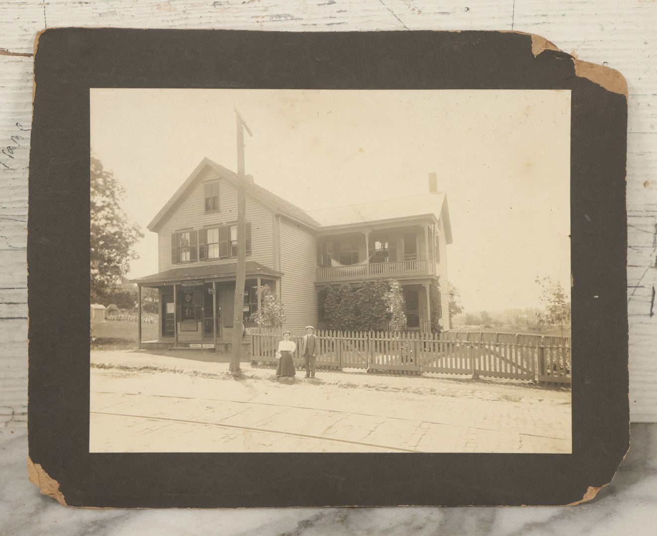 Lot 055 - Antique Boarded Photograph Of A Couple With Dwarfism Posing Outside Of A House / General Store With A Sign Reading "Confectionary, Tonics, Cigars, And Tobacco"