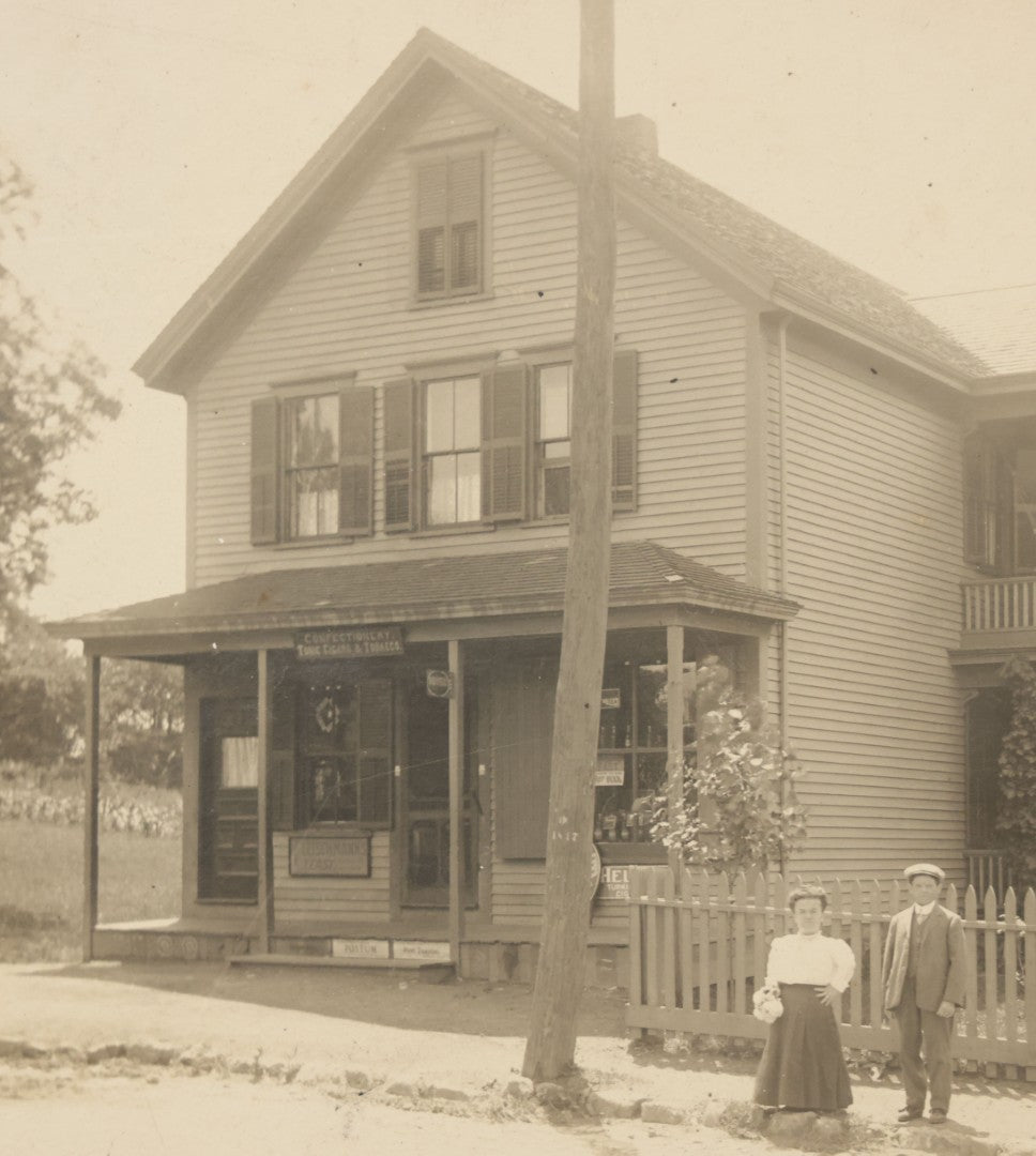 Lot 055 - Antique Boarded Photograph Of A Couple With Dwarfism Posing Outside Of A House / General Store With A Sign Reading "Confectionary, Tonics, Cigars, And Tobacco"
