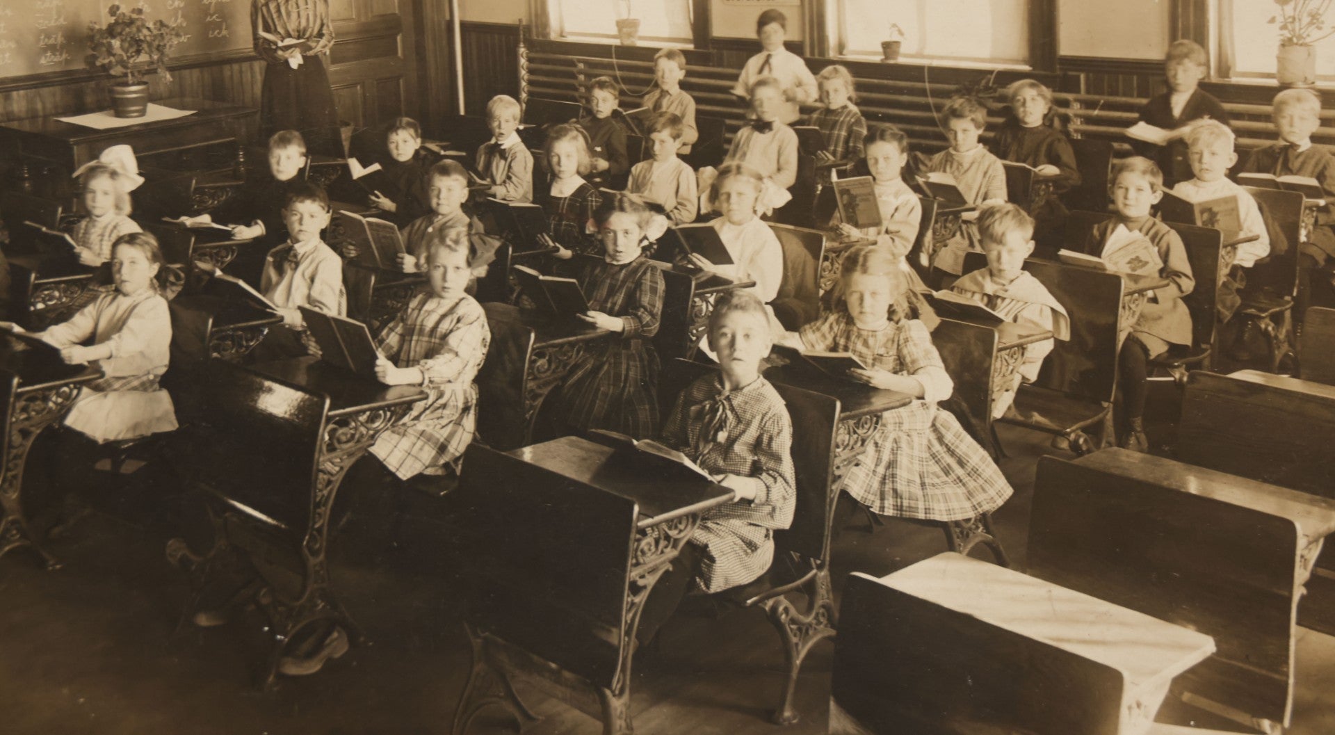 Lot 060 - Antique Boarded Photograph Of The Interior Of A 2Nd Grade Classroom With School Children, Teacher Holding Books,