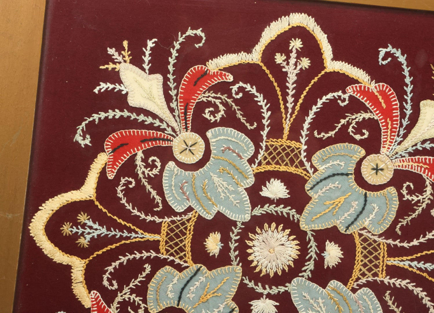 Lot 028 - Vintage Folk Art Needlepoint Embroidery Medallion With Blue, Red, And Yellow Thread On Maroon Field, In Frame