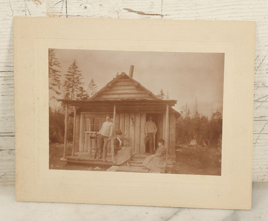Lot 096 - Antique Boarded Photograph Of Two Men And Two Women Posing On The Stoop Of A Hunting Cabin, Men Holding Rifles