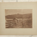 Lot 097 - Antique Boarded Photograph Of Men Holding Rifles, Gamefowl, With Hunting Cabin, Lake, And Mountains In Background