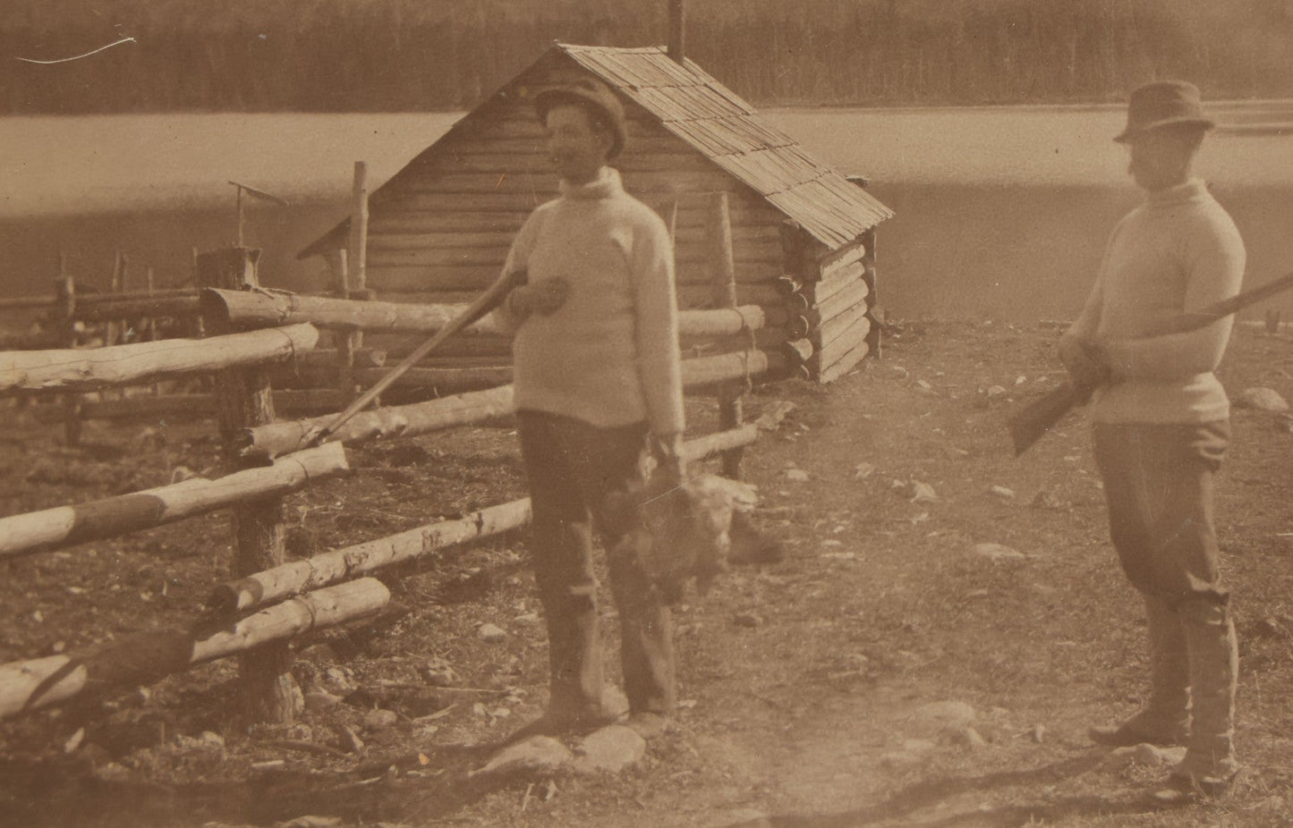 Lot 097 - Antique Boarded Photograph Of Men Holding Rifles, Gamefowl, With Hunting Cabin, Lake, And Mountains In Background