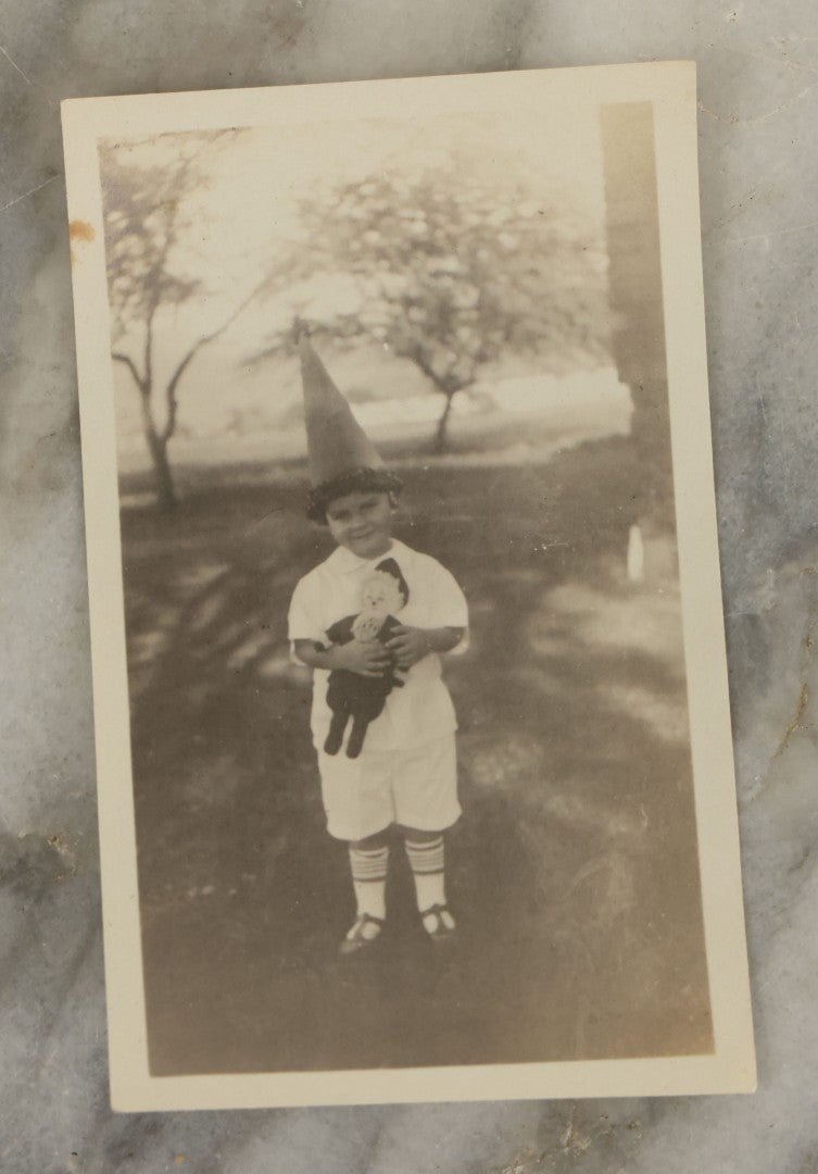 Lot 107 - Single Vintage Snapshot Photograph Of A Young Boy With A Tall Point Hat Holding Stuffed Doll