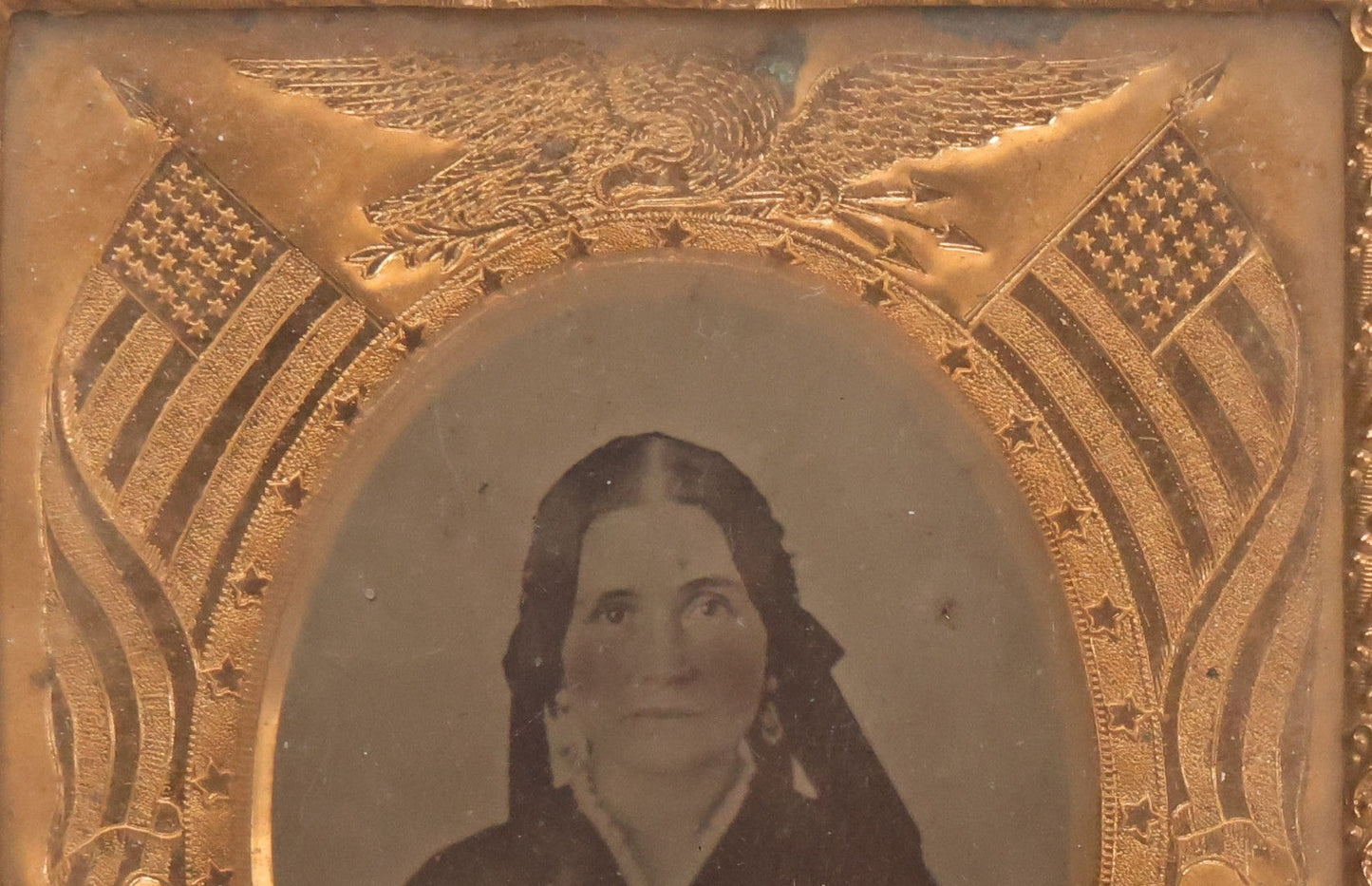 Lot 117 - Antique 1/6th Plate Ambrotype Photograph Of Solemn Woman In Dark Clothing With Patriotic Civil War Era Brass Mat With American Flags, Eagle, Cannon, "E Pluribus Unum" Banner, In Half Case