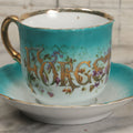 Lot 064 - Antique "Forget Me Not" Porcelain Cup And Saucer With Purple Flowers, Teal Coloring, And Gold Trim, Marked Made In Germany
