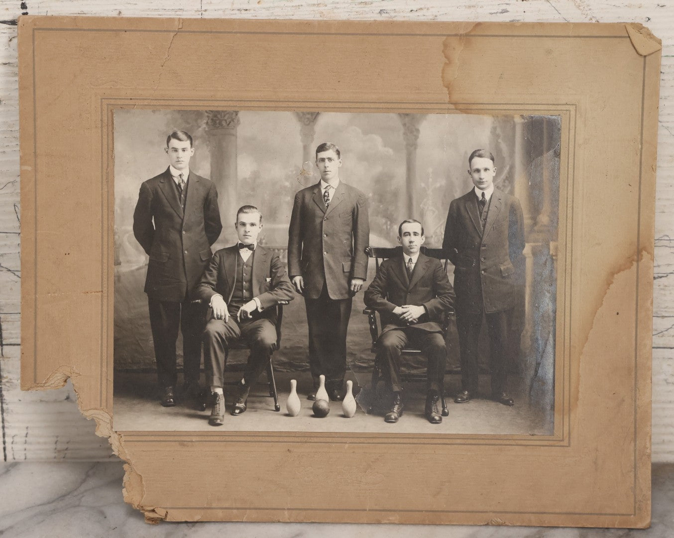 Lot 084 - Antique Boarded Photograph Of Bowling Team Of Five Men Posing With Three Bowling Pins And Bowling Ball, Note Loss To Lower Left Corner, Hole To Left Of Center Mans Head