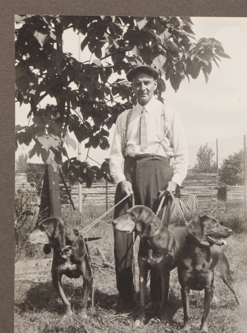 Lot 090 - Vintage Boarded Photograph Of Man In High Waisted Pants With Suspenders Holding Three Hounds On Leashes