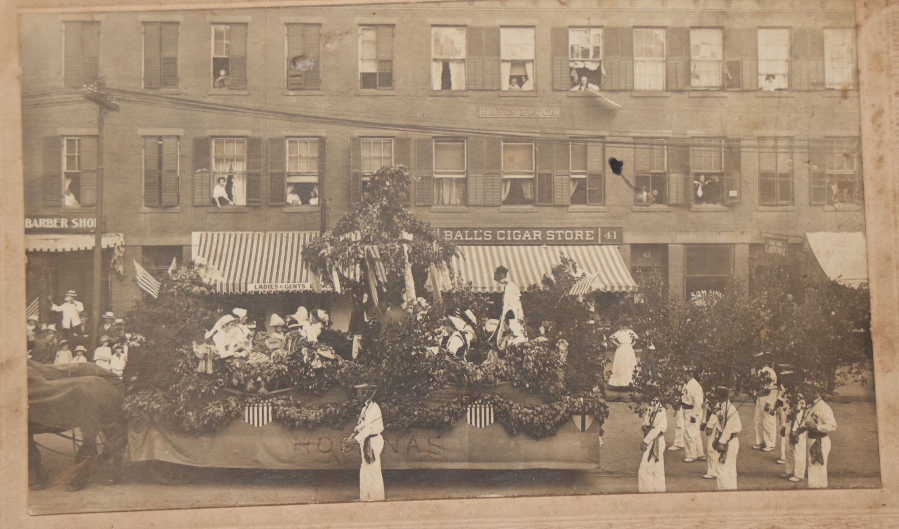 Lot 114 - Antique Boarded Photograph Of Patriotic Parade With Swedish Float With "Hoganas" Banner, Sign On Building "Bangs Block" (Likely Springfield, Mass.), Other Signs "Ball's Cigar Store", "Ladies & Gents Lounge", Barber Shop And "Sam Sing Laundry"
