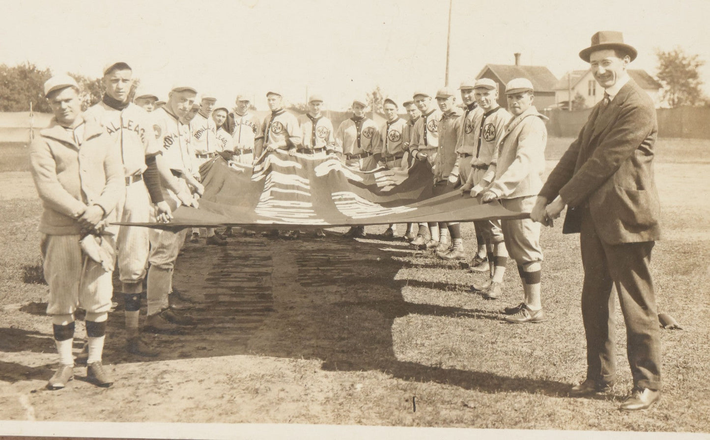Lot 139 - Antique Boarded Photograph Of The Players Of A Baseball Team In Uniform Posing With A Large Flag, Uniforms Say "Royal League" With Patches Visible
