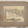 Lot 142 - Antique Boarded Occupational Photograph Of Men And Women Workers Posing In Workwear Outside A Barn, Women In Bowler Hats And Bonnets And Man Smoking Pipe
