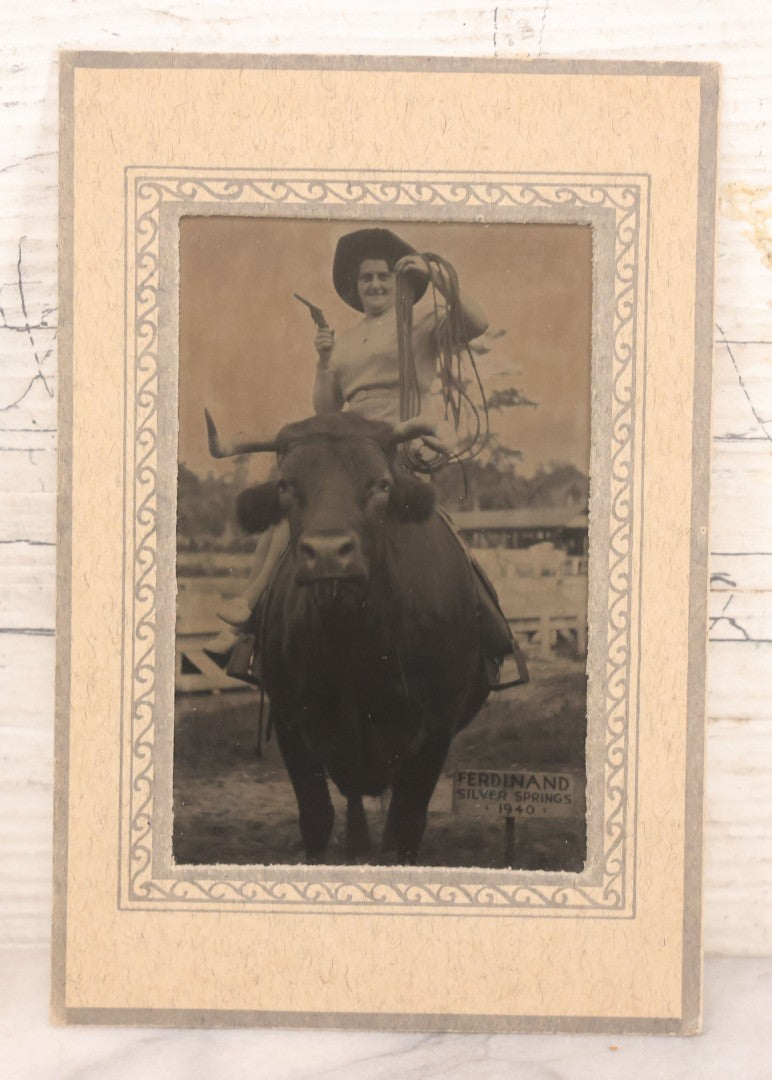 Lot 092 - Pair Of Vintage Souvenir Photographs Of Man And Woman Posing With Revolver, Cowboy Hat, And Lasso, Sitting On Back Of Horned Bull, Souvenir Of Ferdinand Silver Springs, 1940