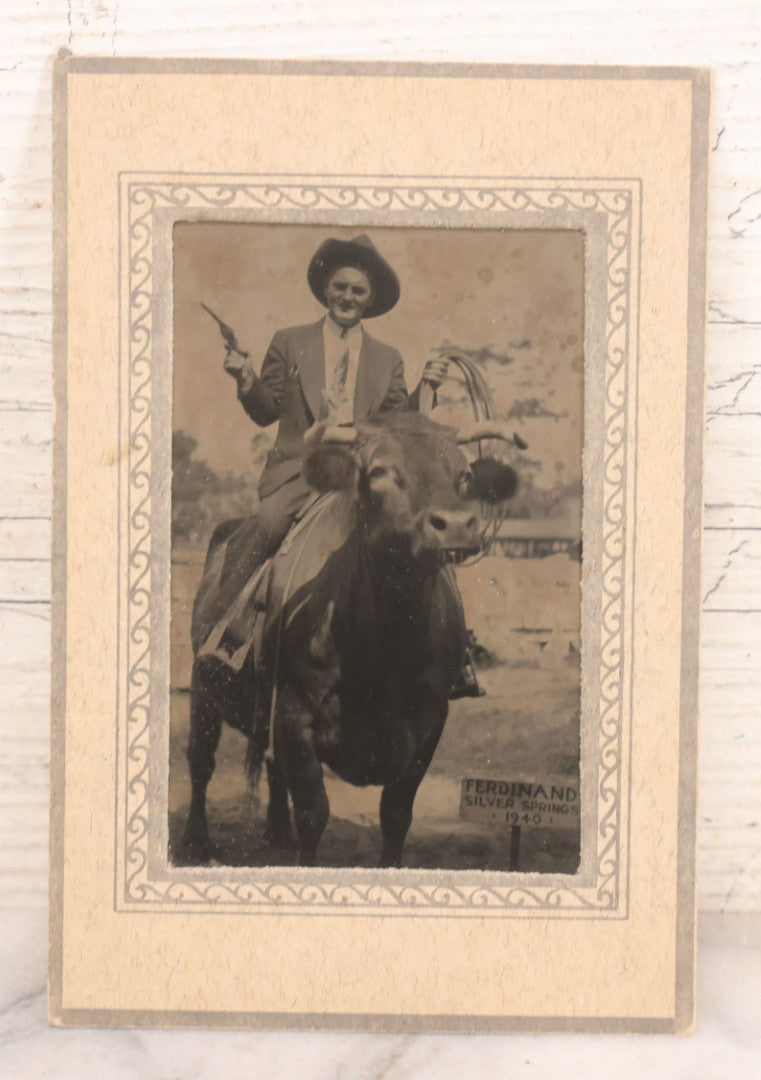 Lot 092 - Pair Of Vintage Souvenir Photographs Of Man And Woman Posing With Revolver, Cowboy Hat, And Lasso, Sitting On Back Of Horned Bull, Souvenir Of Ferdinand Silver Springs, 1940