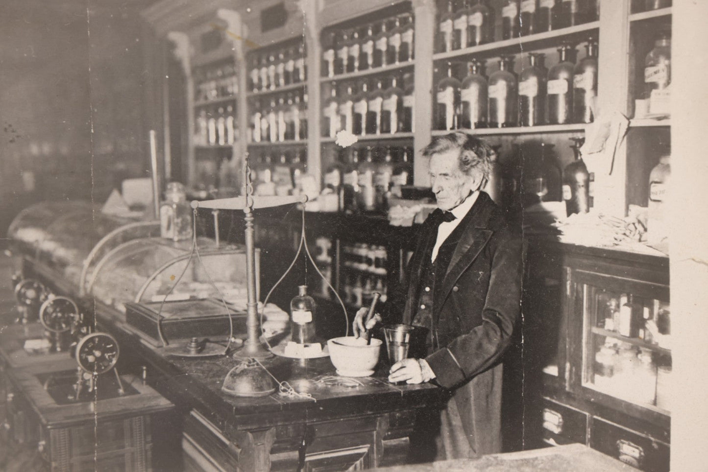 Lot 093 - Antique Large Format Photograph Of Elderly Pharmacist Compounding Medicine At The Pharmacy Counter, With Many Apothecary Bottles And Tools Visible