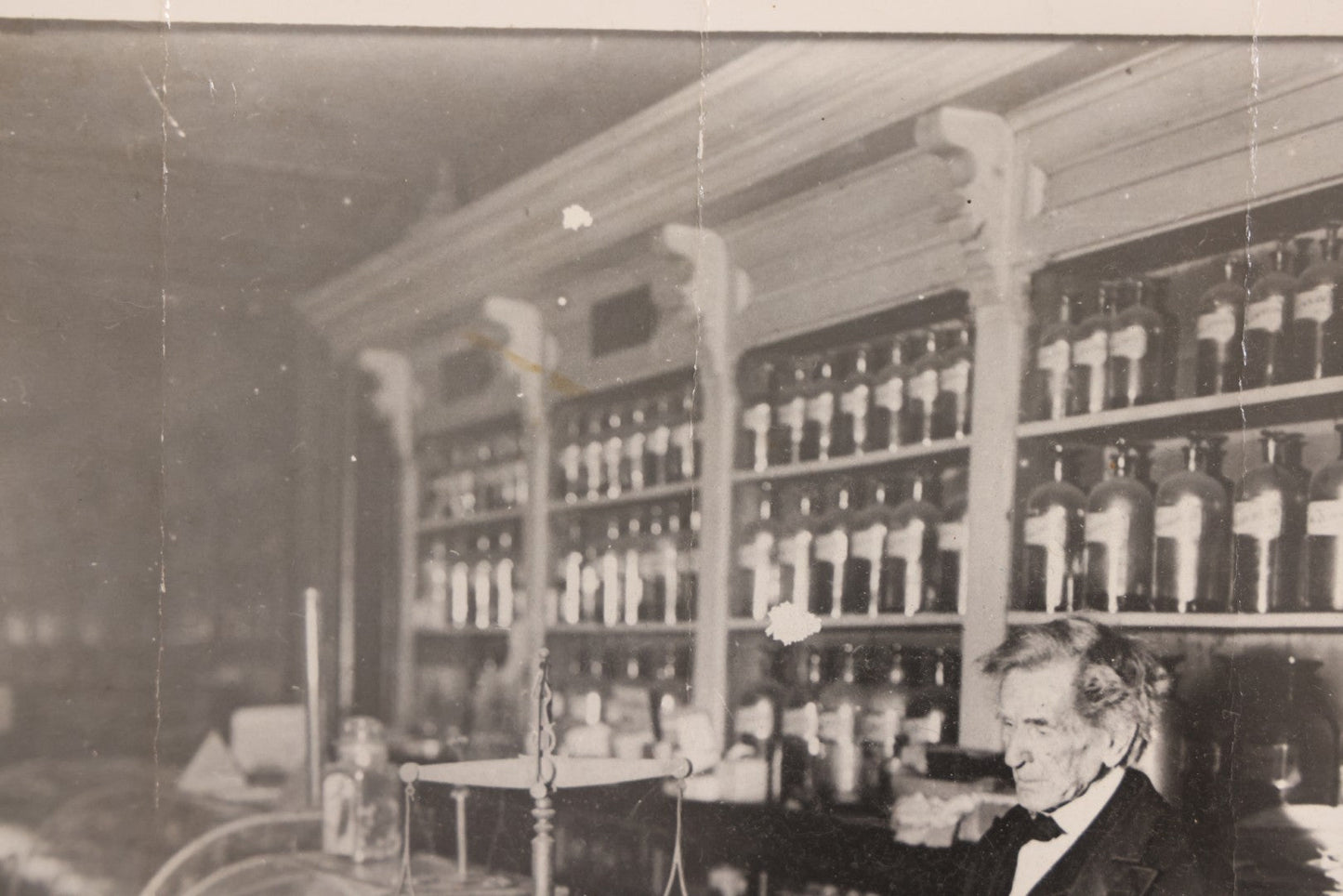 Lot 093 - Antique Large Format Photograph Of Elderly Pharmacist Compounding Medicine At The Pharmacy Counter, With Many Apothecary Bottles And Tools Visible