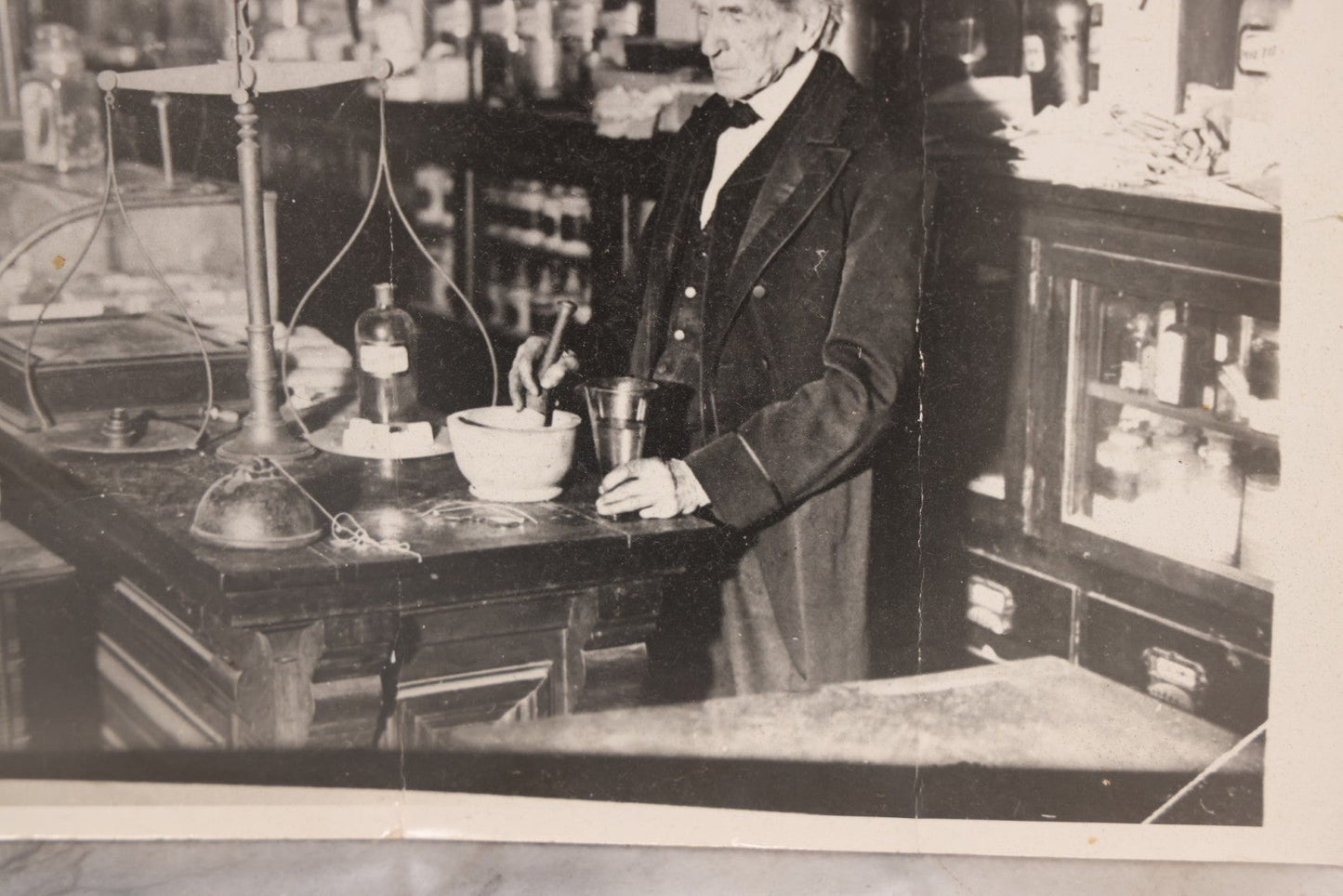 Lot 093 - Antique Large Format Photograph Of Elderly Pharmacist Compounding Medicine At The Pharmacy Counter, With Many Apothecary Bottles And Tools Visible