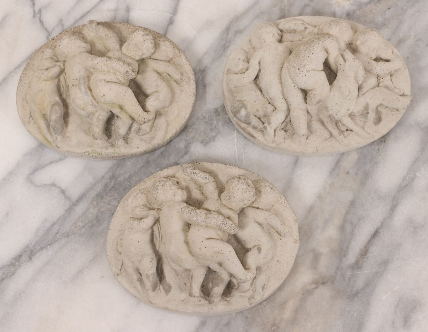 Lot 078 - Grouping Of Three Vintage Concrete Wall Plaques Depicting Cherubs In Different Scenes, Including With Lamb