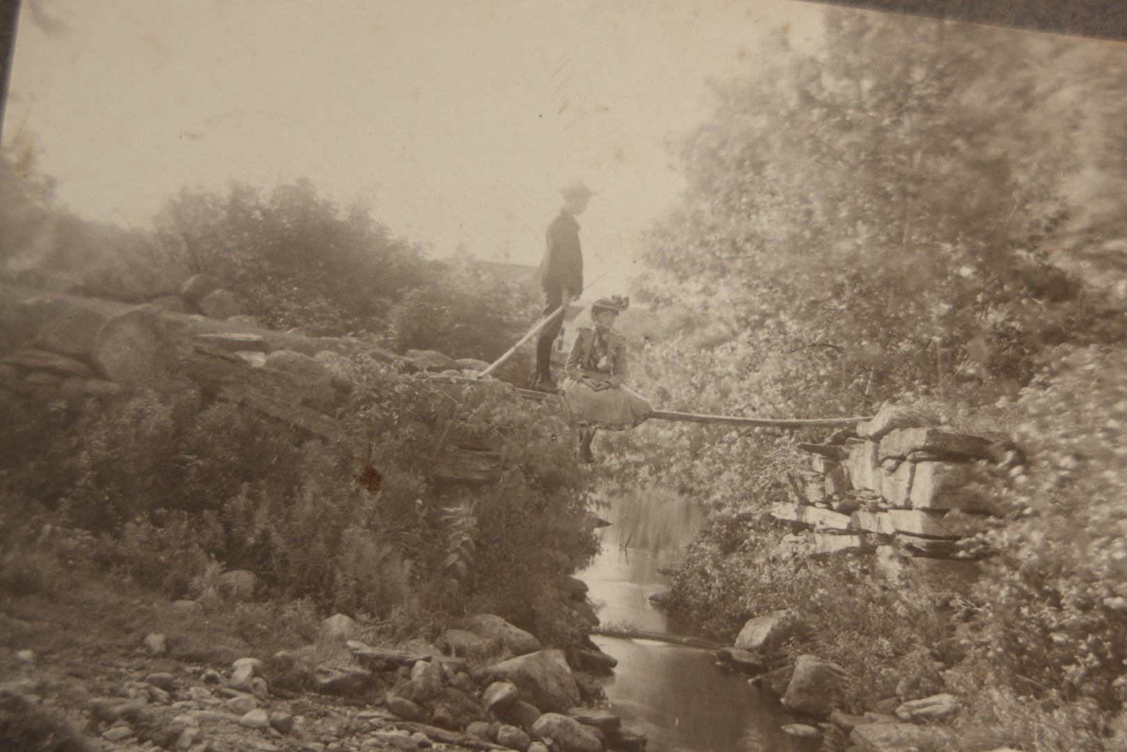 Lot 131 - Pair Of Antique Boarded Photographs Of Outdoor Scenes, Including Boy And Girl On Primitive Stick Bridge Crossing Creek, Canoe