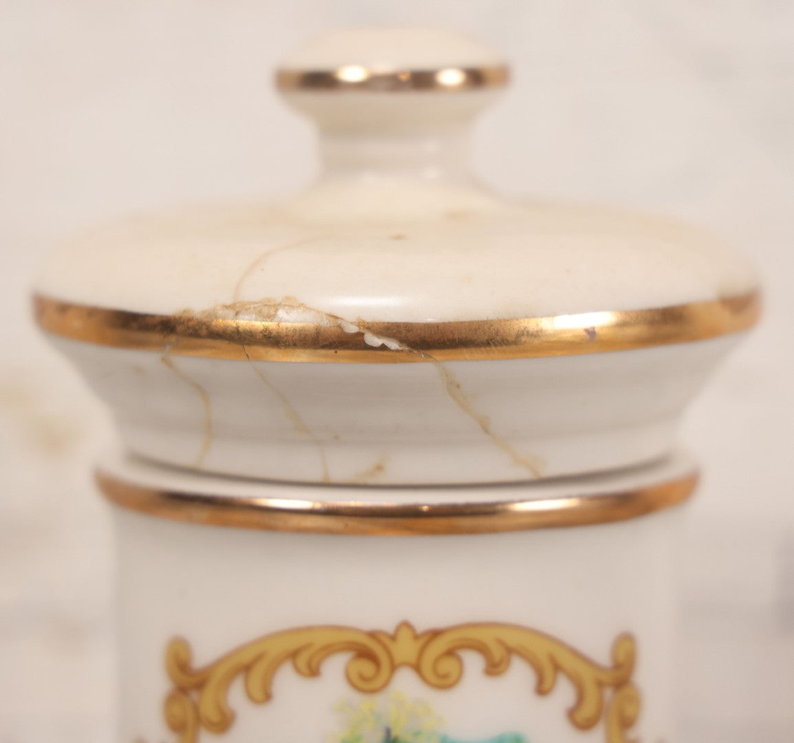 Lot 084 - Reproduction Fantasy Apothecary Jar With Lid Marked “Nux Vomica” White Opaque Pottery With Gold Painted Lines, Mid-20th Century, Bottom Marked Made In U.S.A., Note Broken And Repaired Lid, 7-5/8" H