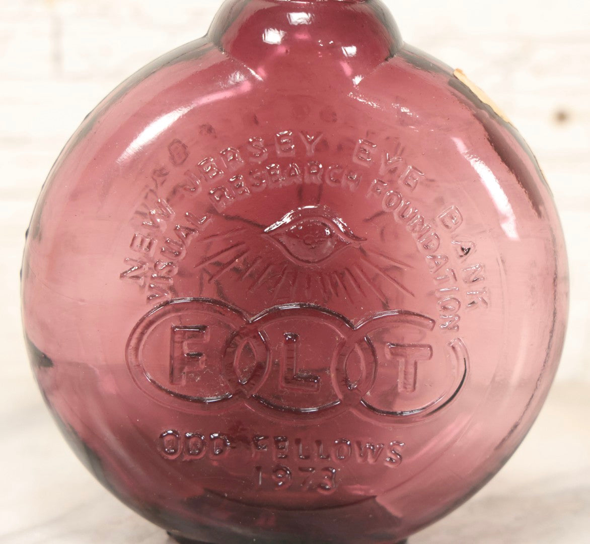 Lot 114 - Vintage Odd Fellows And Rebekah Commemorative Purple Glass Bottle, “New Jersey Eye Bank Visual Research Foundation,” 1973, With All-Seeing-Eye And F.L.T. Three Links, Clevenger Bros. Glass Works, Clayton, New Jersey, 7" H