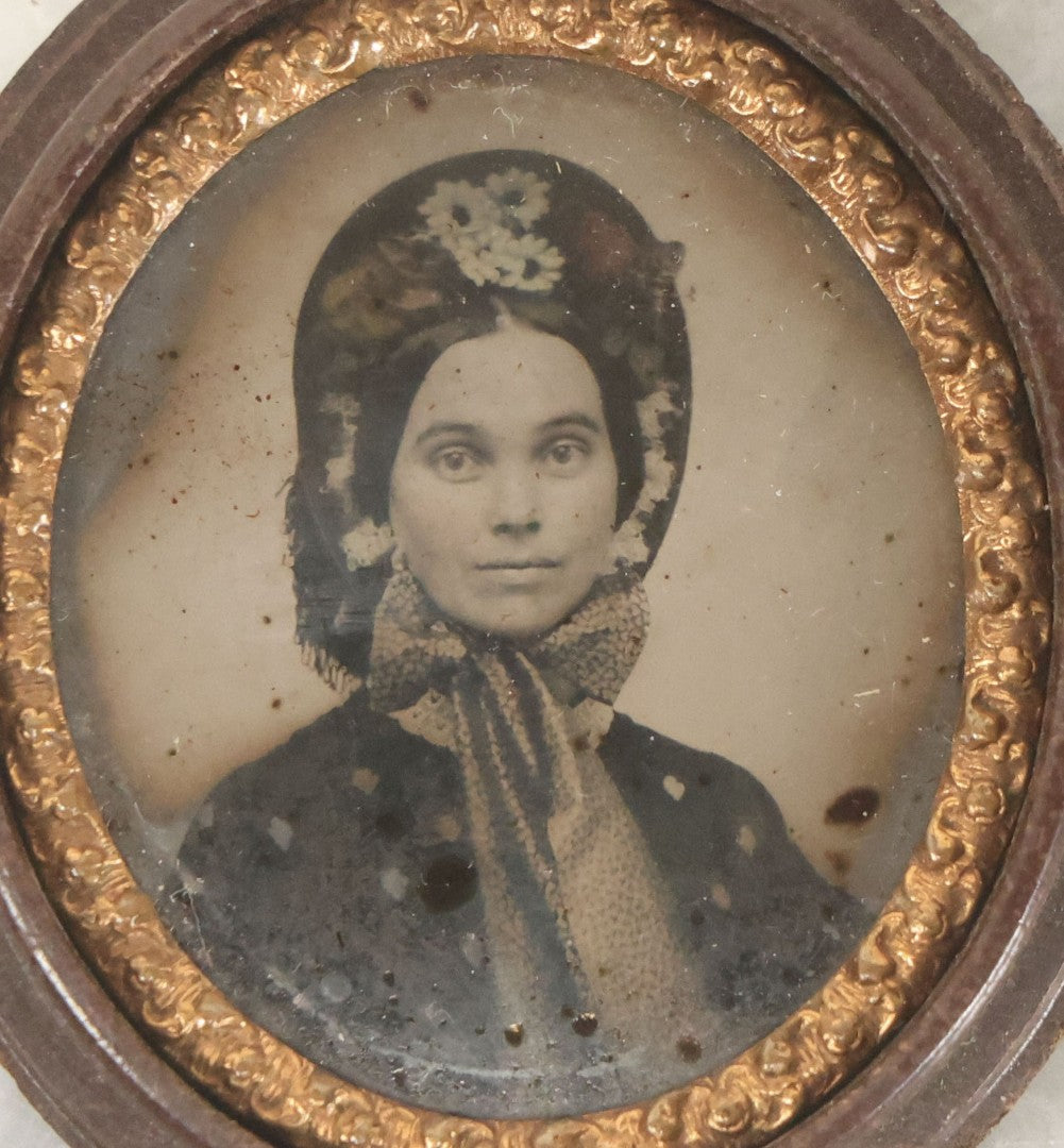 Lot 164 - Antique Oval-Cut Tintype Photograph Of Woman In Bonnet With Flowers And Bow Scarf, In Brown Thermoplastic “Oreo”-Style Case With Brass Preserver, 1-7/8" x 2-1/8"