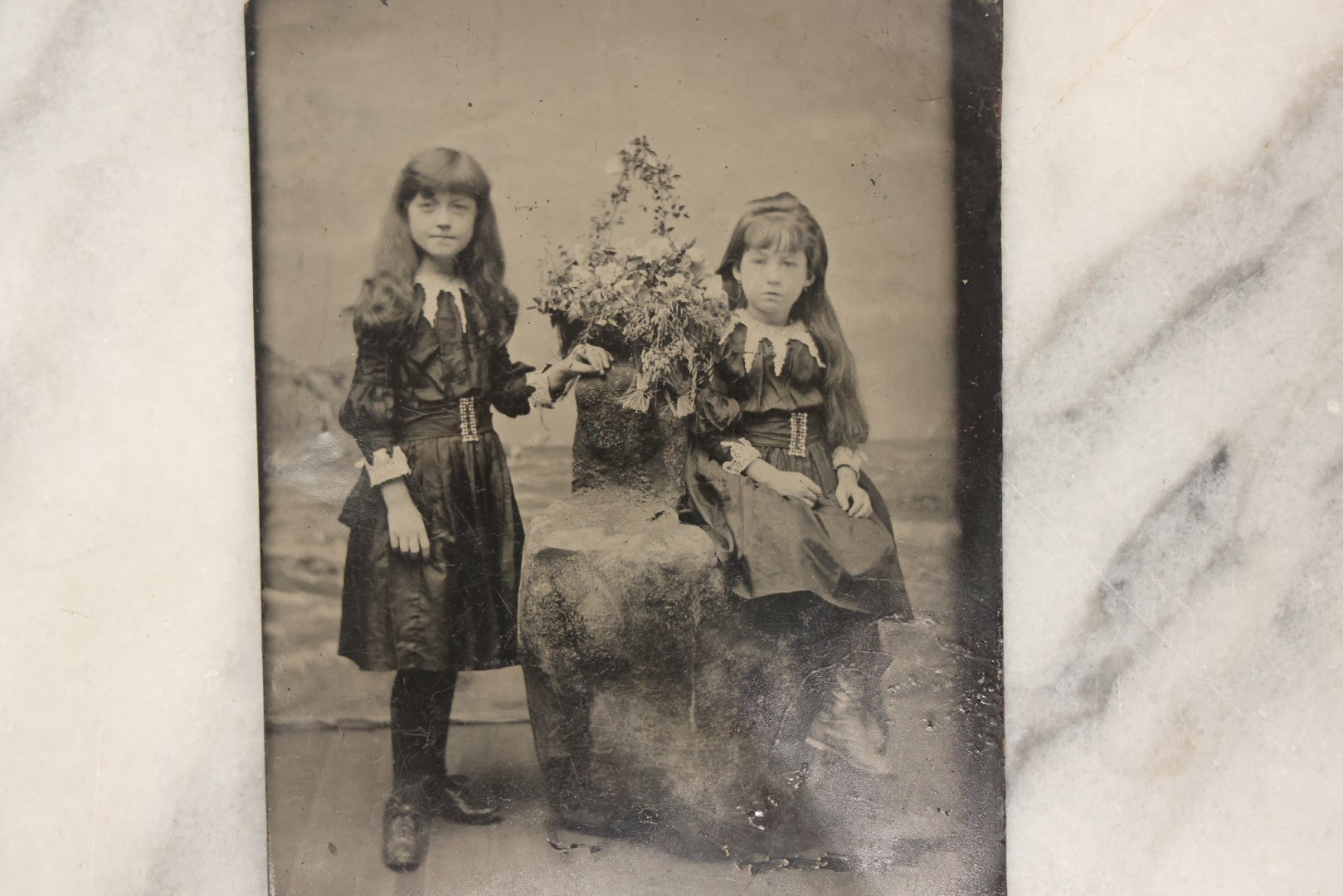 Lot 166 - Antique 1/4 Plate Tintype Photograph Of Two Young Girls In Matching Dresses Posed In Studio Beach Scene With Floral Bouquet And Coastal Background