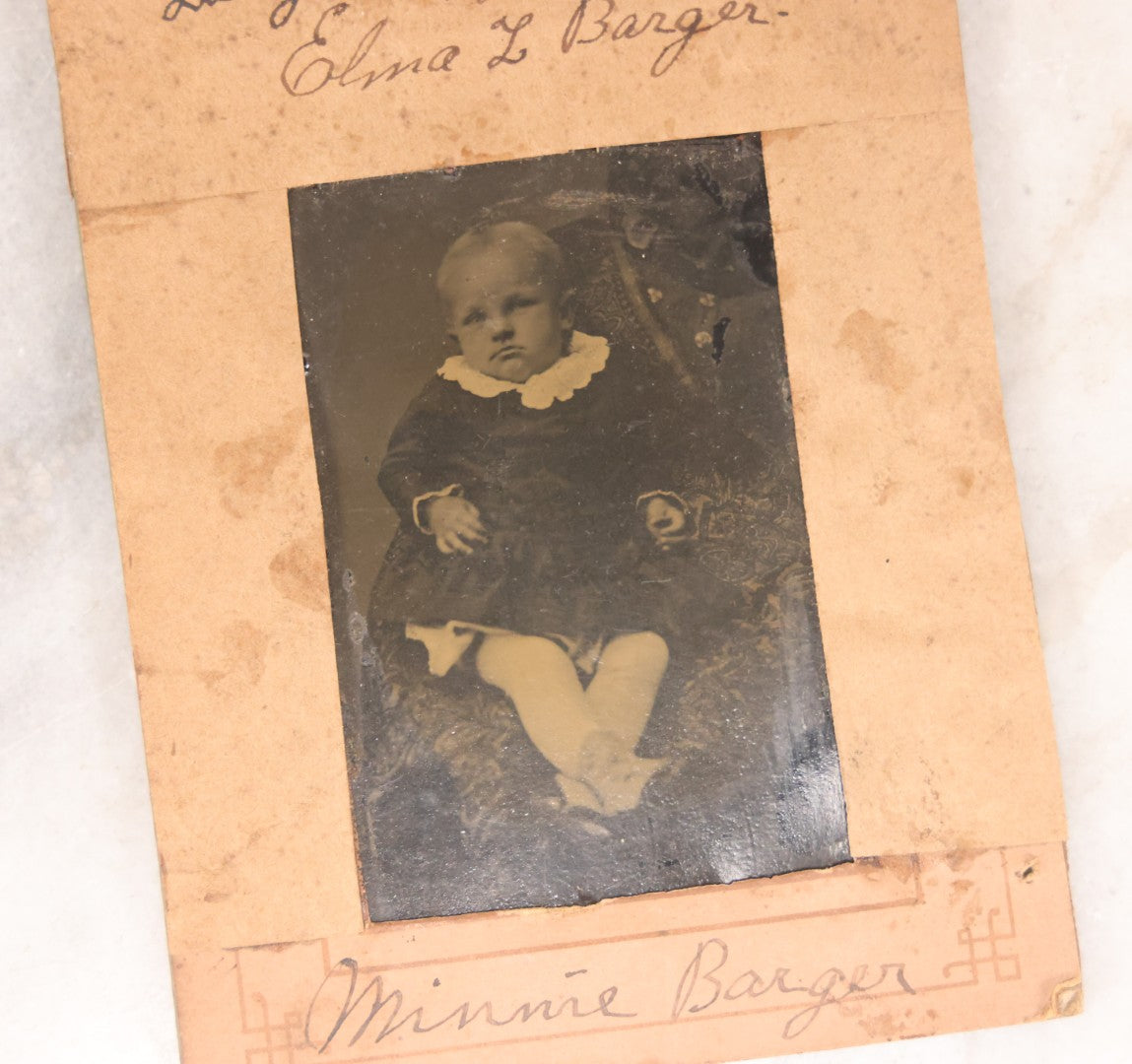 Lot 087 - Antique Tintype Photograph Of Baby In Mother's Lap, A “Not-So-Hidden Mother” Portrait, Identified As Minnie Barger, Daughter Of John J. And Elma L. Barger, In Makeshift Paper Frame