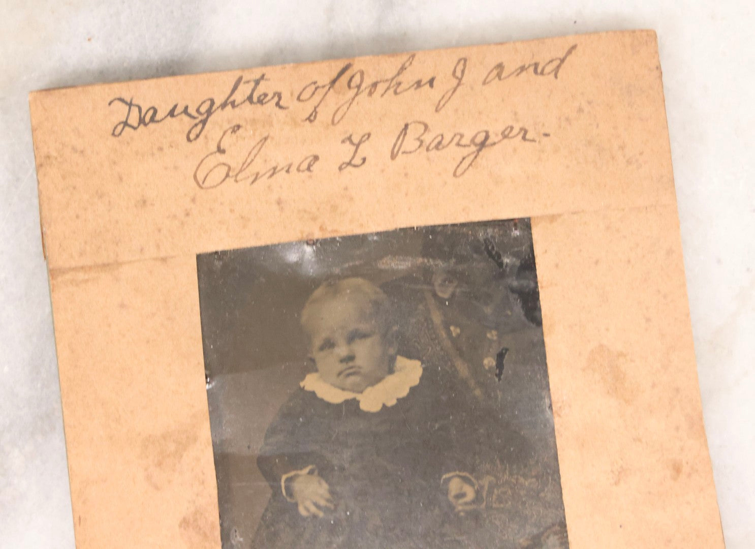 Lot 087 - Antique Tintype Photograph Of Baby In Mother's Lap, A “Not-So-Hidden Mother” Portrait, Identified As Minnie Barger, Daughter Of John J. And Elma L. Barger, In Makeshift Paper Frame