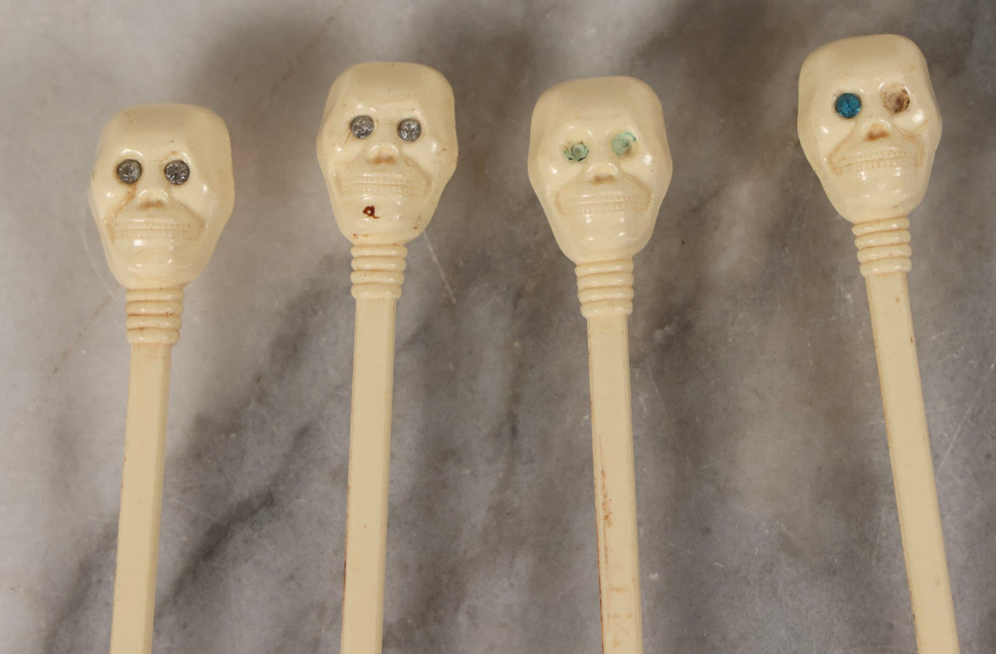 Lot 095 - Grouping Of Four Vintage Molded Plastic Skull-And-Bone Swizzle Stick Cocktail Stirrers With Rhinestone Eyes, Circa 1950s–1960s 6-3/4" L Each