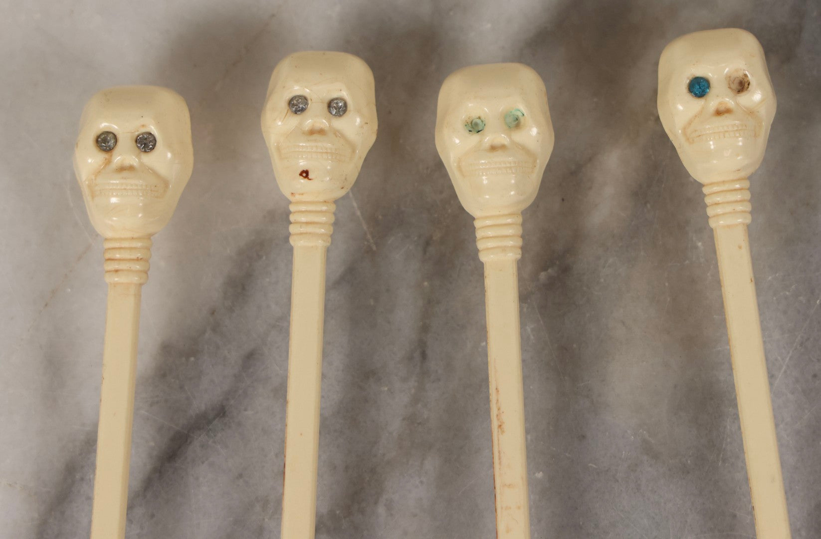 Lot 095 - Grouping Of Four Vintage Molded Plastic Skull-And-Bone Swizzle Stick Cocktail Stirrers With Rhinestone Eyes, Circa 1950s–1960s 6-3/4" L Each