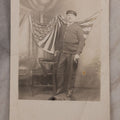 Lot 174 - Antique Real Photo Postcard R.P.P.C. Of Man In Uniform And Cap With Cigarette Before American Flag Backdrop, Circa 1910s