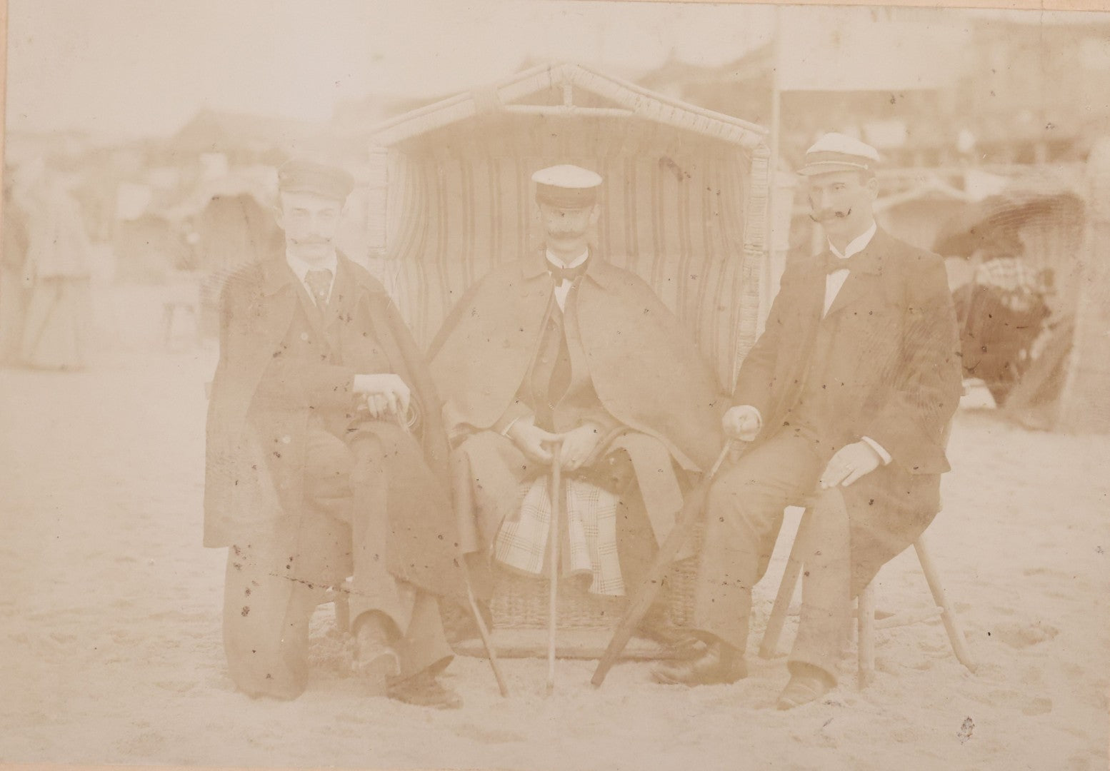 Lot 179 - Antique Board-Mounted Photograph Of Three Mustachioed Men Posed On Beach In Suits With Capes And Walking Sticks Before Striped Beach Windbreak, Westerland, Sylt, Photographed By A. Gabel