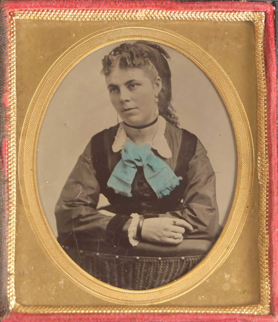 Lot 077 - Antique 1/6th Plate Tintype Photograph, Portrait Of A Young Woman With Hand-Tinted Blue Bow And Ringlet Curls, In Half Leatherette Case