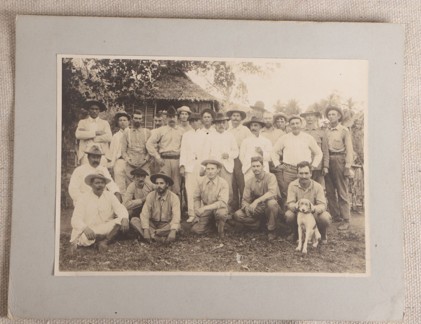 Lot 096 - Antique Board-Mounted Photograph Of A Group Of Men In A Tropical Setting With A Dog