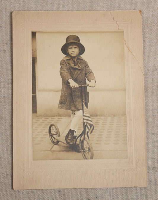 Lot 104 - Antique Board-Mounted Photograph Of A Child On A Kick Scooter With American Flag