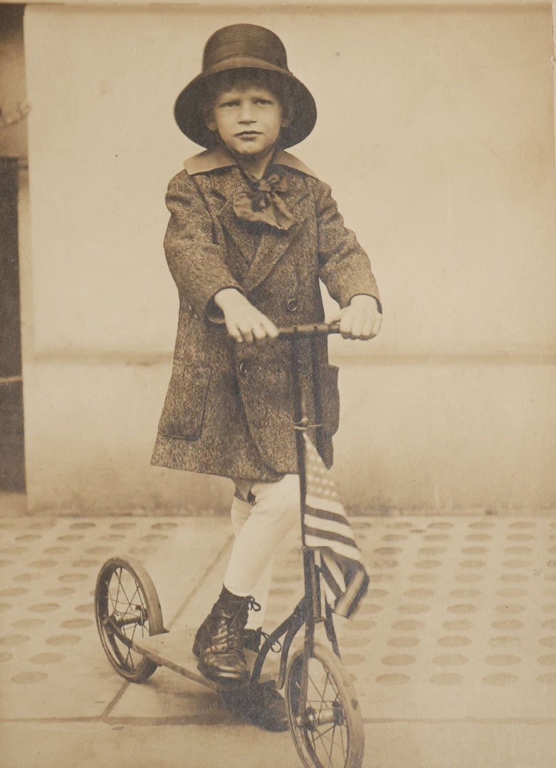 Lot 104 - Antique Board-Mounted Photograph Of A Child On A Kick Scooter With American Flag