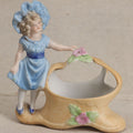 Lot 177 - Antique Bisque Figural Vase With Girl In Blue Dress Beside A Flower-Adorned Basket, Likely German, 4-1/2" Height