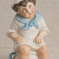 Lot 181 - Antique Bisque Figure of a Child With White Hat Seated on a Chamber Pot, Likely German, 4-3/8" Height