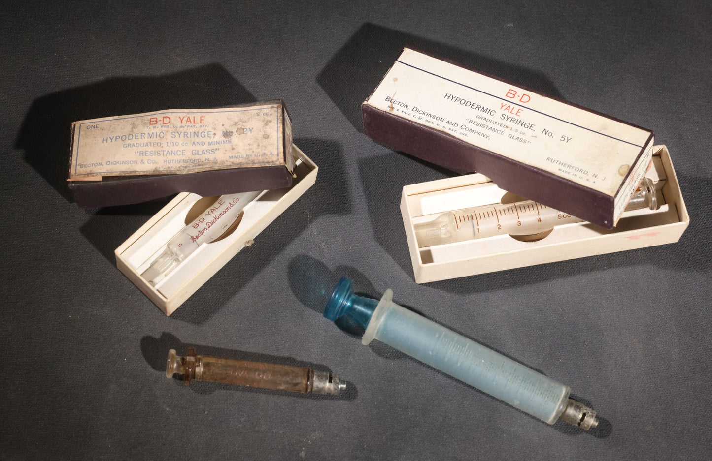 Lot 012 - Grouping Of Four Vintage Glass Medical Syringes Including Two Boxed B-D Yale Hypodermic Syringes By Becton, Dickinson And Company, Rutherford, New Jersey, One Propper Mfg. Co. 10Cc Syringe, And One B-D Yale Luer-Lok Syringe