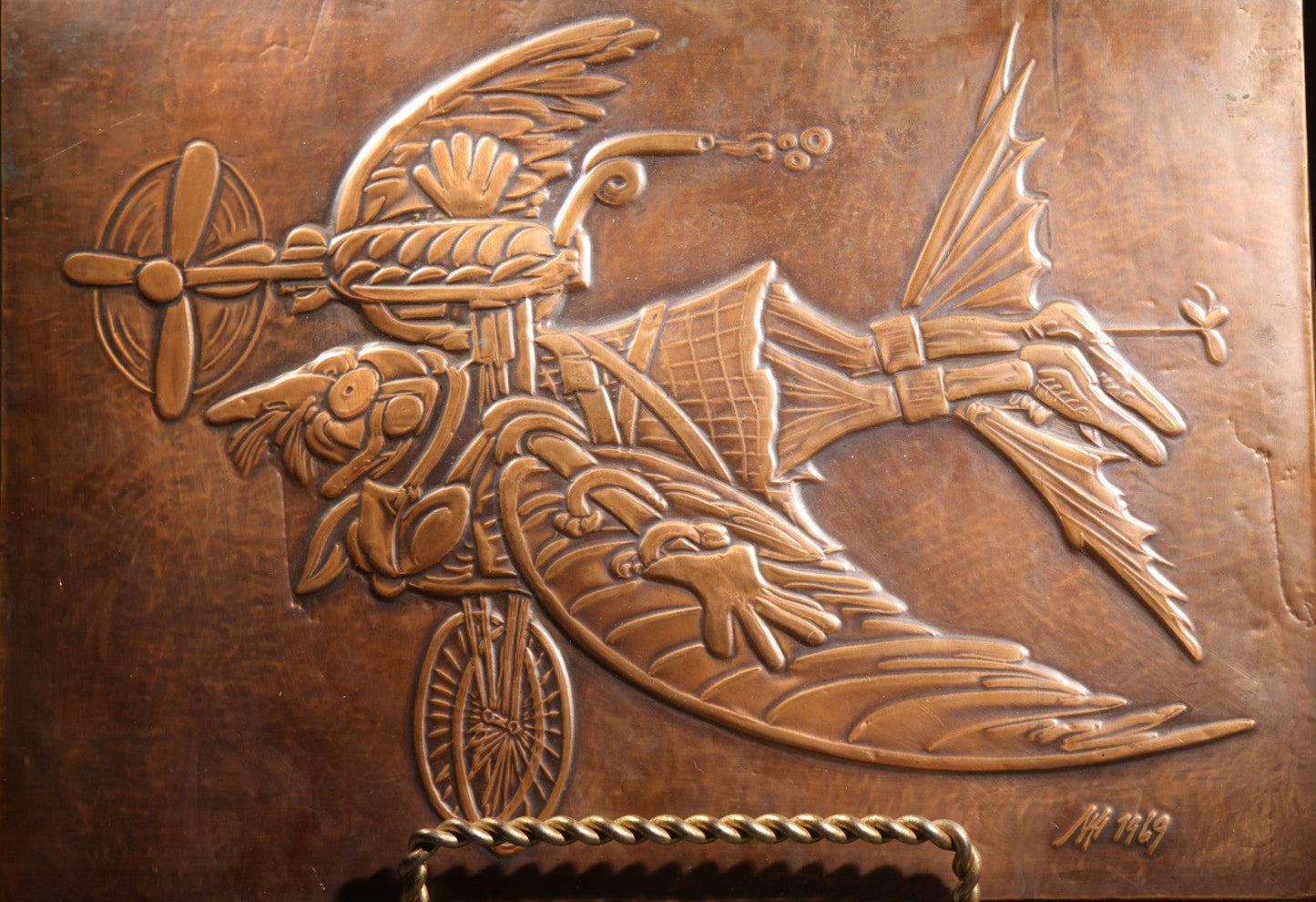 Lot 051 - Vintage Copper Repoussé Plaque On Plywood, Fantastical Winged Figure On Unicycle With Propeller, Signed And Dated 1969, Gifted From Reck, Germany, 1972, 9-1/4" x 13"